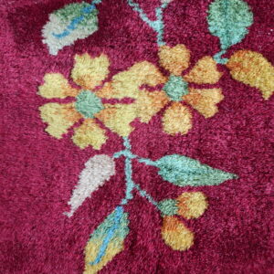 Plush burgundy rug with a detailed floral design featuring yellow, green, cream, and blue accents.