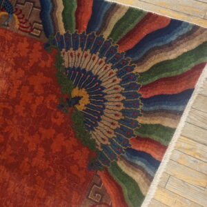 Red and multicolored rug with a large fan design shown on light plank wooden floors.