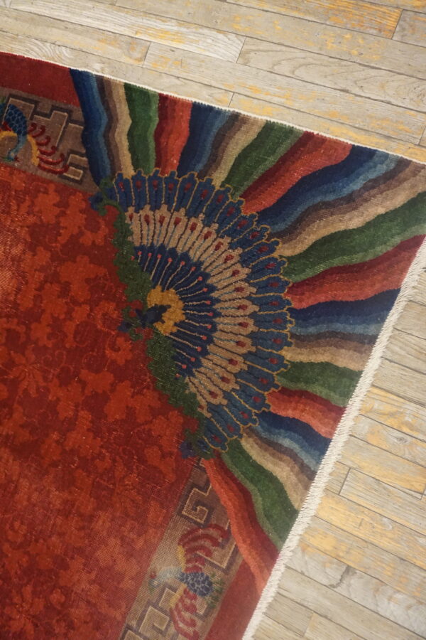 Red and multicolored rug with a large fan design shown on light plank wooden floors.