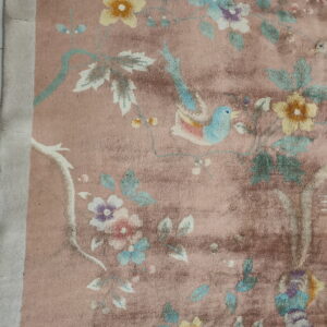 Distressed dusty rose rug featuring multicolored flowers, vines, and a light blue bird pattern.