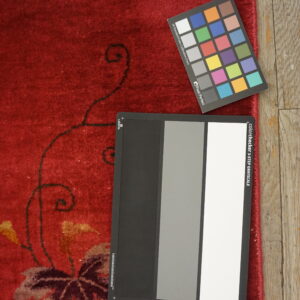 Textured, plush red rug with large autumnal leaf patterns rests next to worn wood flooring.