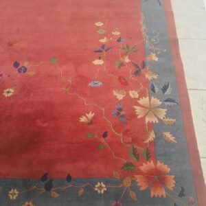 Terracotta rug with a colorful floral and vine design bordered by slate gray, placed on white tile.