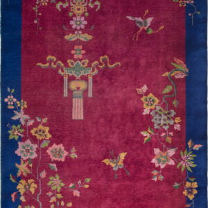 A deep berry red rug with a dark blue border, adorned with colorful floral vines and central symbols.