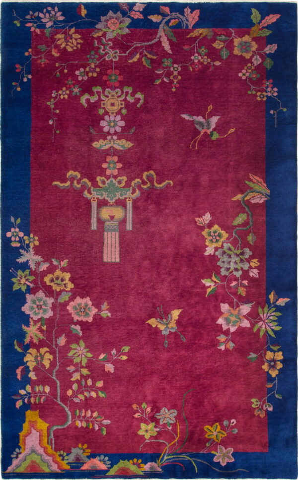 A deep berry red rug with a dark blue border, adorned with colorful floral vines and central symbols.