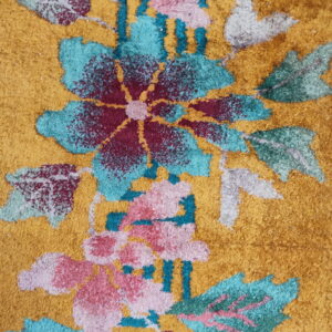 Detail view of a mustard yellow cut-pile rug with large stylized flowers in teal, maroon, and pink.