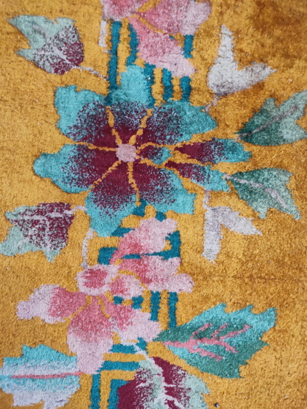 Detail view of a mustard yellow cut-pile rug with large stylized flowers in teal, maroon, and pink.