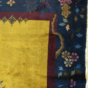 Yellow high-pile rug detail showing a navy floral border separated by a deep maroon guard stripe.