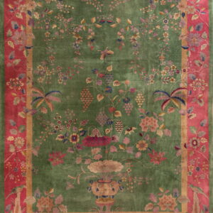 Green rug featuring a detailed multicolored floral pattern, purple grapes, and a wide magenta border with birds.