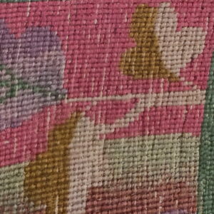 Close-up of flatweave rug showing magenta, lavender, and green stylized floral motifs.