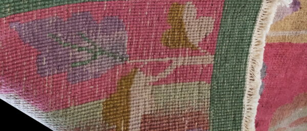 Close-up of flatweave rug showing magenta, lavender, and green stylized floral motifs.