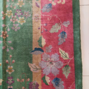 Intricate floral vine pattern covers green and magenta striped panels of a textured rug on tile.