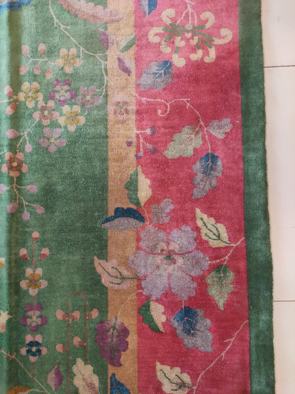 Intricate floral vine pattern covers green and magenta striped panels of a textured rug on tile.