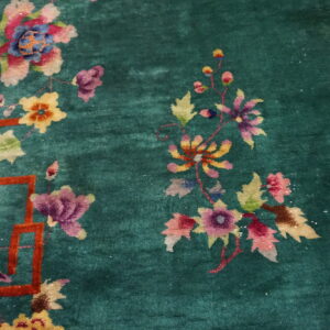 Close-up of a high-pile emerald rug featuring multicolored floral designs and an orange geometric lattice border.
