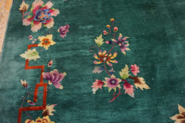 Close-up of a high-pile emerald rug featuring multicolored floral designs and an orange geometric lattice border.