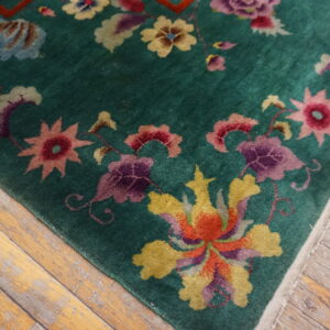 Deep green rug with large multicolored floral designs lying on worn, light wood planks.