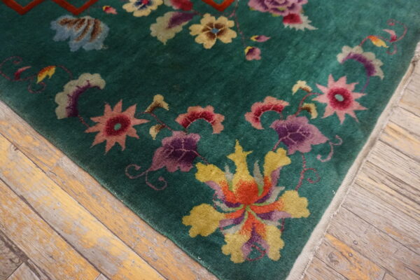 Deep green rug with large multicolored floral designs lying on worn, light wood planks.