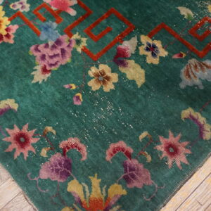 Teal rug with vibrant floral designs and a red geometric border rests on distressed wooden floorboards.