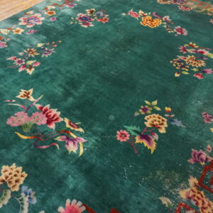 Plush green rug with colorful floral motifs and a red geometric border resting on wood planks.