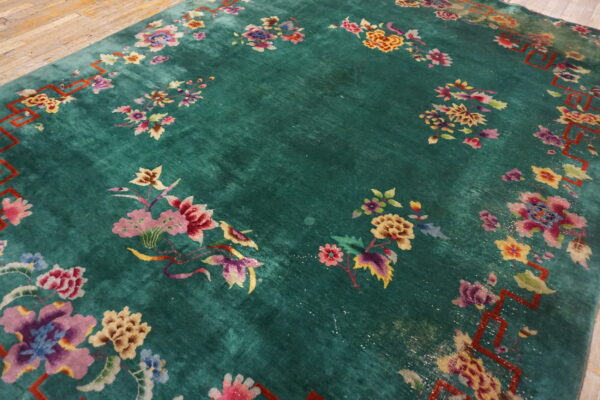 Plush green rug with colorful floral motifs and a red geometric border resting on wood planks.