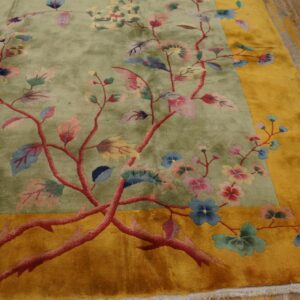 A plush sage green rug with pink floral vines and a wide yellow border rests on wood planks.