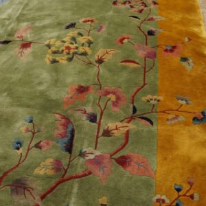 High-pile green rug with multicolor floral vines and a wide gold border on distressed wood floor.