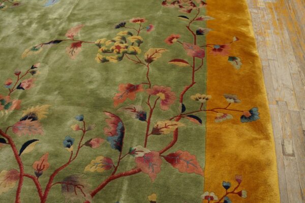 High-pile green rug with multicolor floral vines and a wide gold border on distressed wood floor.