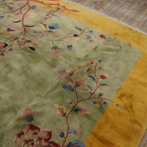 Olive green floral rug with a gold border rests on distressed gray wood flooring.