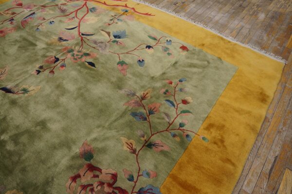 Olive green floral rug with a gold border rests on distressed gray wood flooring.