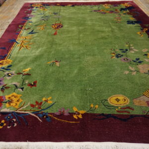 Vibrant green rug with a deep red border and detailed multicolored floral patterns lies on a wood floor.