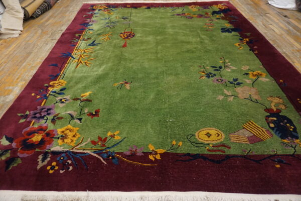 Vibrant green rug with a deep red border and detailed multicolored floral patterns lies on a wood floor.