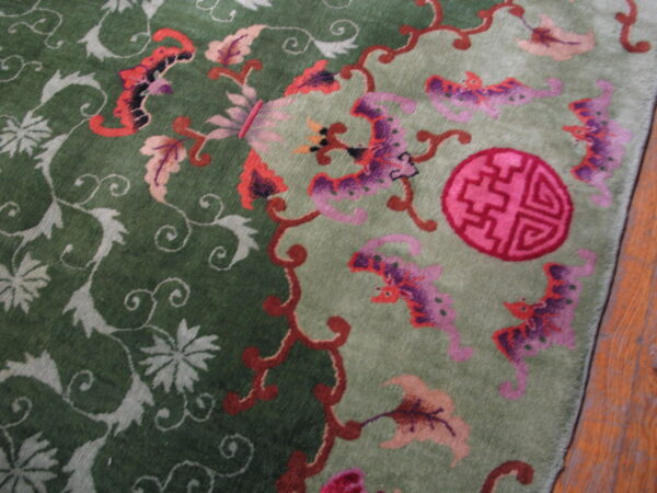 Dark and light green plush rug with contrasting pink and red ornate floral and bat motifs on wood floor.