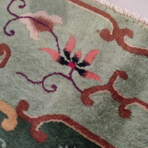 High-pile rug with a sage green field and stylized floral patterns in pink, red, and dark green.