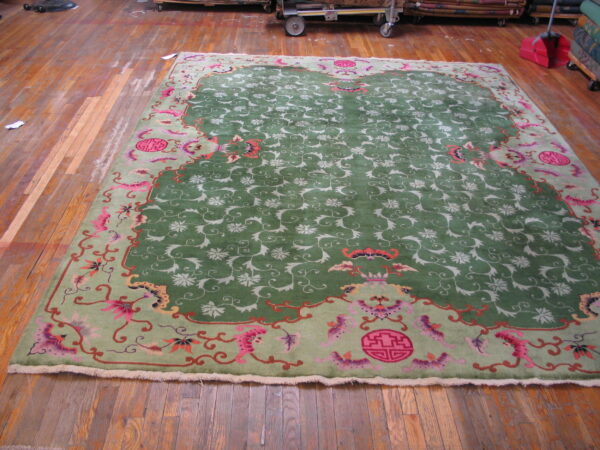 A large green rug with a pink and light green border sits on a distressed wood floor near storage carts.
