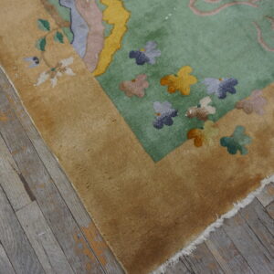 Tan-bordered rug with a light green field and multi-colored floral designs rests on distressed wood flooring.