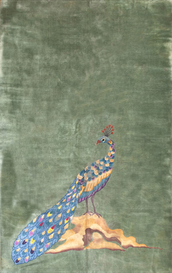 A distressed sage green rug features a large, multicolor peacock design standing on a brown and tan rock.