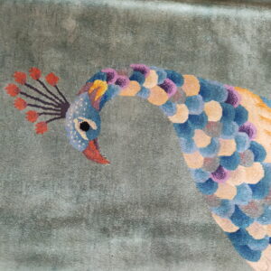 Detail of a rug showing a multicolor peacock design against a subtly textured sage green background.