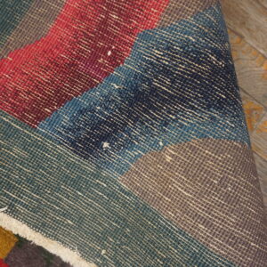 A rolled rug displays red, blue, and teal flatweave foundation over a dark brown, low pile surface.