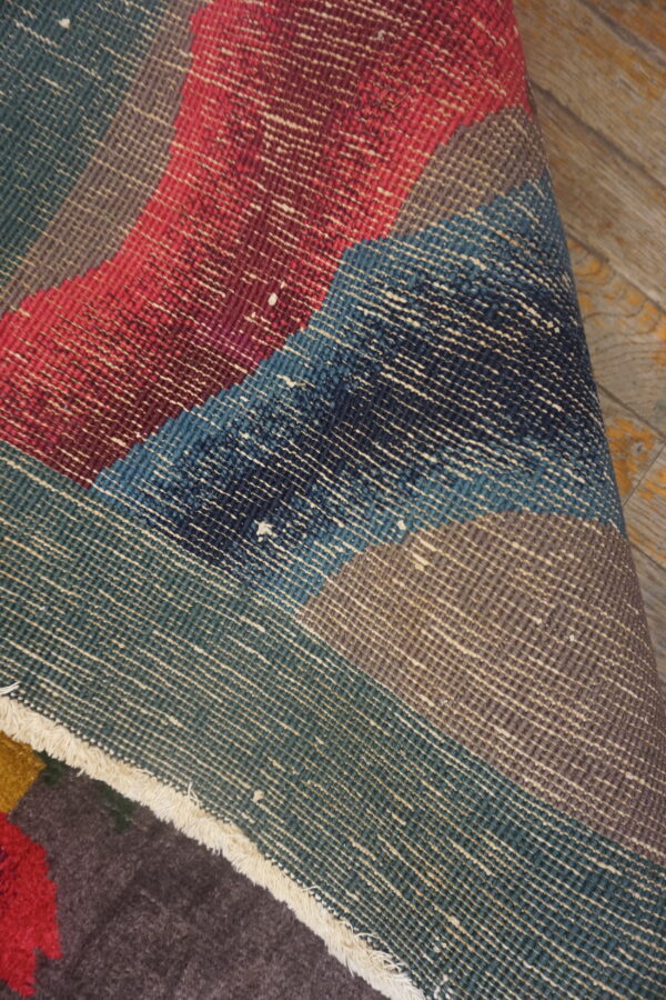 A rolled rug displays red, blue, and teal flatweave foundation over a dark brown, low pile surface.