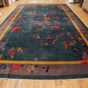 Dark teal rug with colorful birds and flowers, featuring a wide taupe and gold striped border on a wood floor.