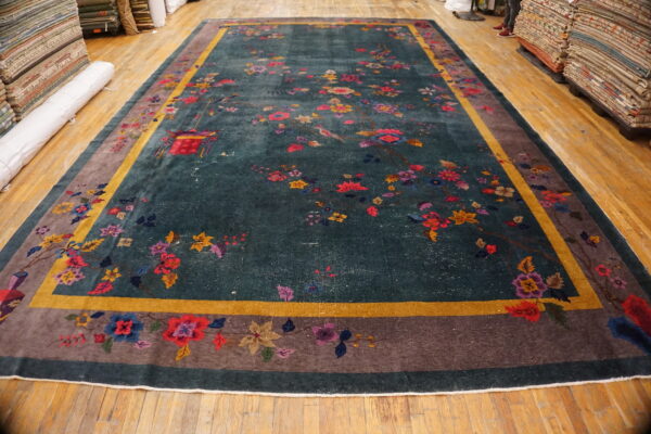 Dark teal rug with colorful birds and flowers, featuring a wide taupe and gold striped border on a wood floor.