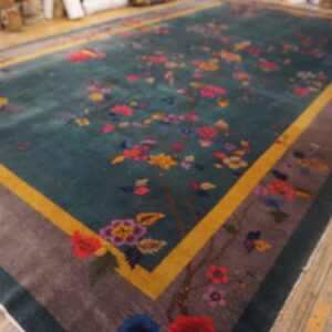 Colorful floral rug with a teal field and gold and taupe border displayed on wooden floorboards.