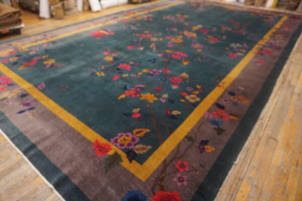 Colorful floral rug with a teal field and gold and taupe border displayed on wooden floorboards.