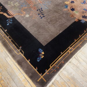 High-pile rug with a taupe center and black, stylized floral border resting on worn wood planks.