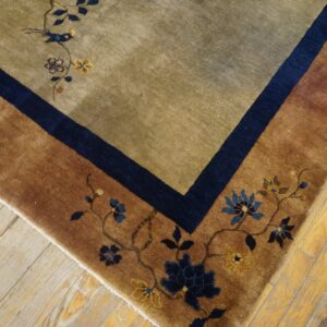 A brown and olive rug with blue floral details and bird pattern rests on worn wood flooring.