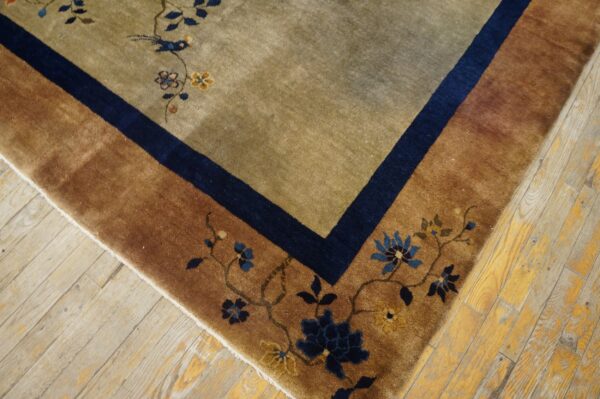 A brown and olive rug with blue floral details and bird pattern rests on worn wood flooring.
