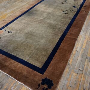 A low-pile taupe rug with rust borders and navy floral patterns rests on a distressed wood floor.