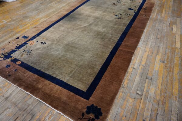 A low-pile taupe rug with rust borders and navy floral patterns rests on a distressed wood floor.
