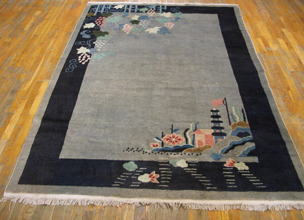 Gray pictorial rug with dark navy border features asymmetric vines and a detailed pagoda landscape on wood floor.