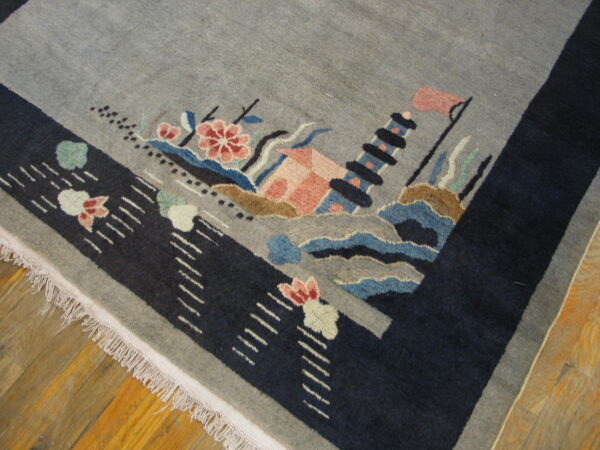 Gray rug corner with a navy border and fringe, displaying a multicolored scenic design on wood floors.