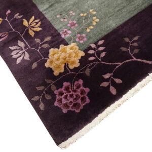 Floral rug detail showing a dark plum border with large flowers bordering a lighter green field.